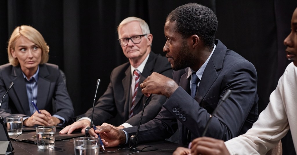 A man speaking into a microphone to other committee members during a meeting.