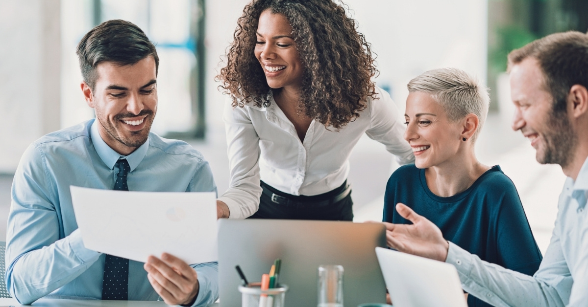 Four coworkers smiling and laughing together, while looking at a document.