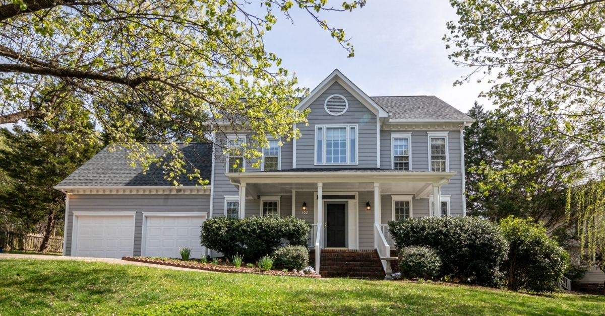 Outside view of the front of a two story house with trees and foliage surrounding the perimeter.