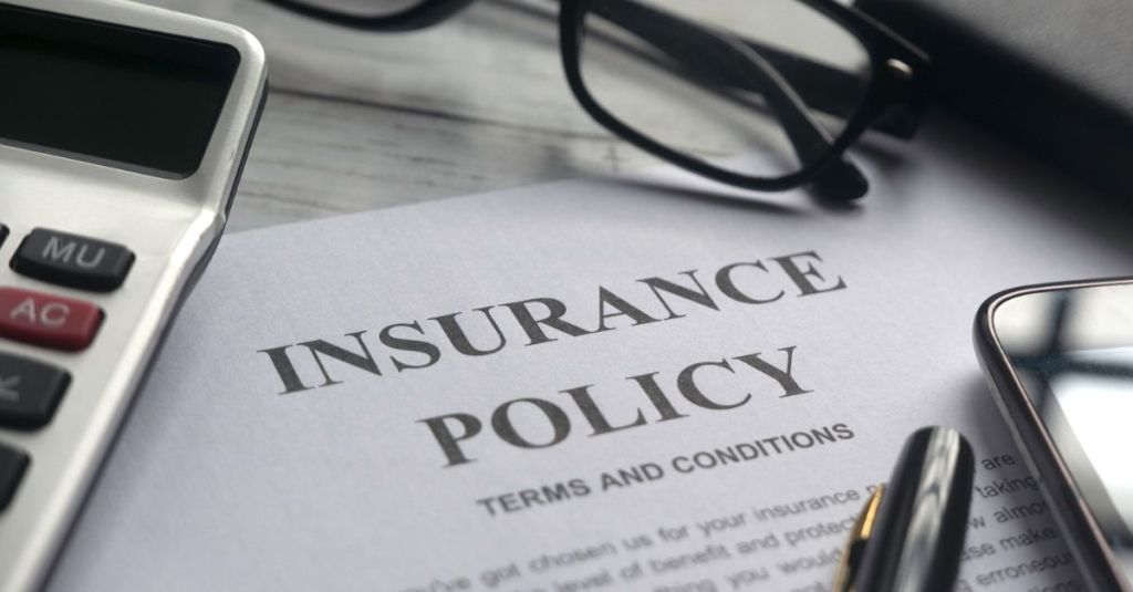 "Insurance Policy" types on paper with a calculator, glasses, pen, and phone surrounding it.