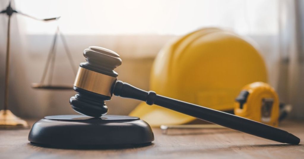 A gavel sitting in front of a yellow hard hat and a tape measure.
