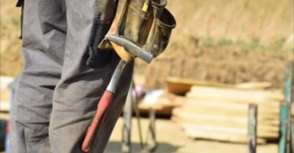 Person standing in a construction site with the focus on the hammer on their tool belt