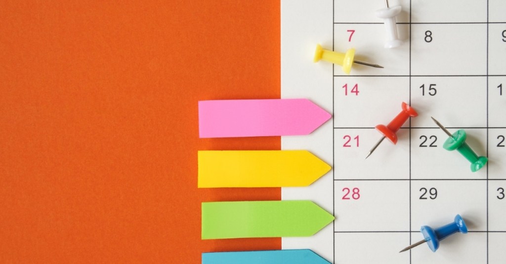A close-up view of the side of a calendar with sticky notes and push pins scattered on it.