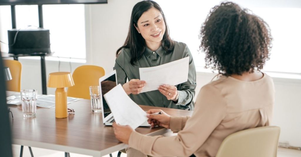 A woman smiling at another woman across the table during a meeting.