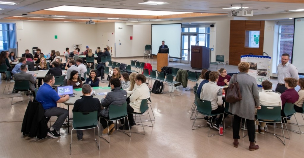 Wide shot view of a room full of students and presenters at the Invest Field Trip 2025 at Le Moyne College.