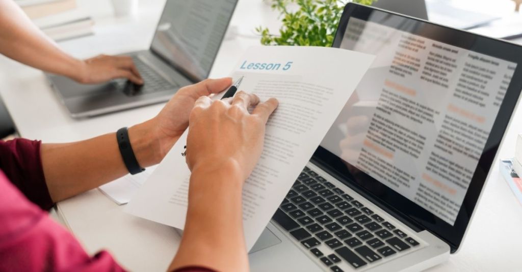 A person studying a lesson plan document with a laptop in front of them.
