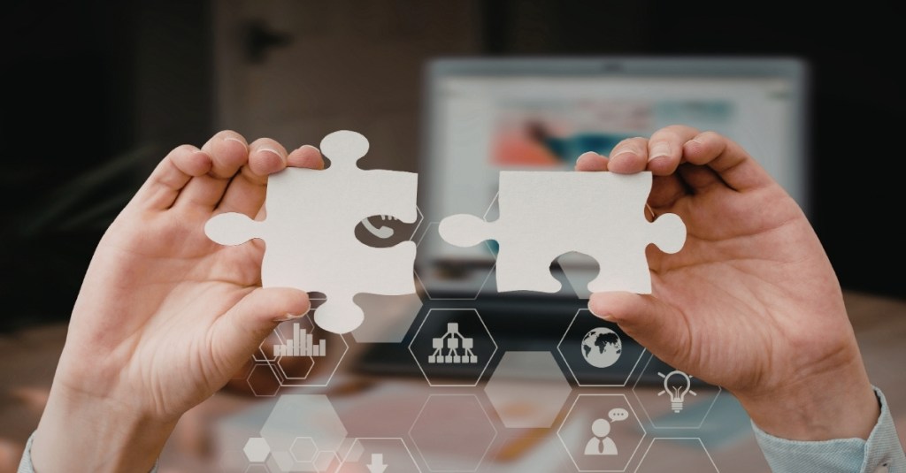 Two hands putting together two puzzle pieces.