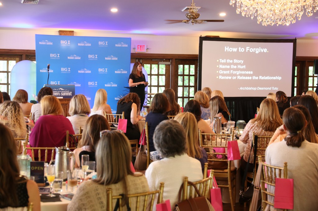 Claudia St. John The Leadership Skill We Don’t Talk About Enough in front of her slide about How to Forgive speaking to the crowd of women attendees