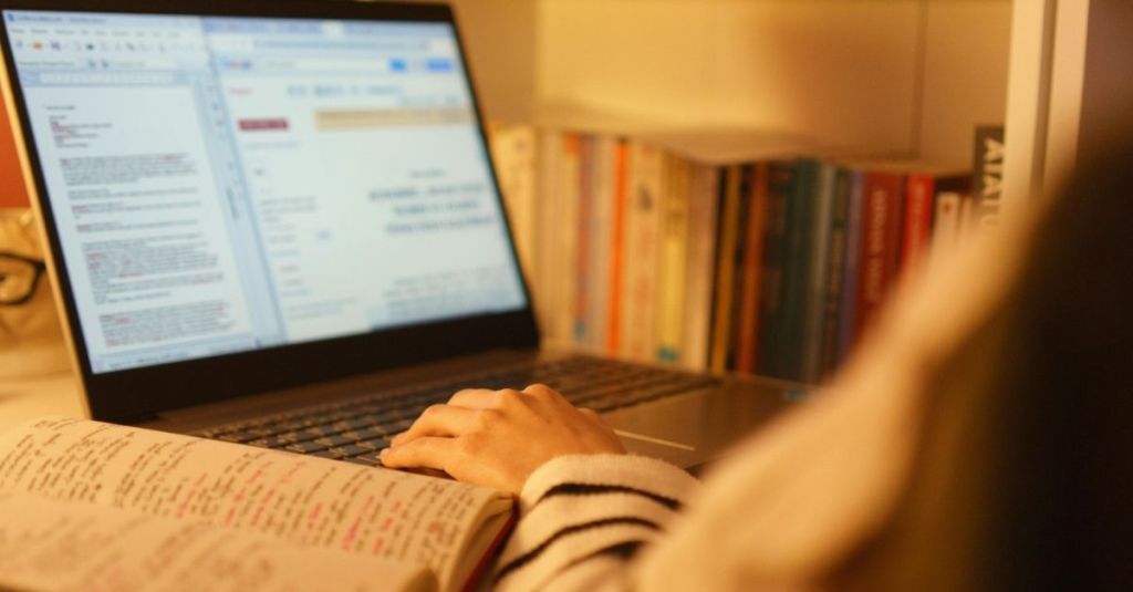 A person working on a laptop with a notebook beside them.