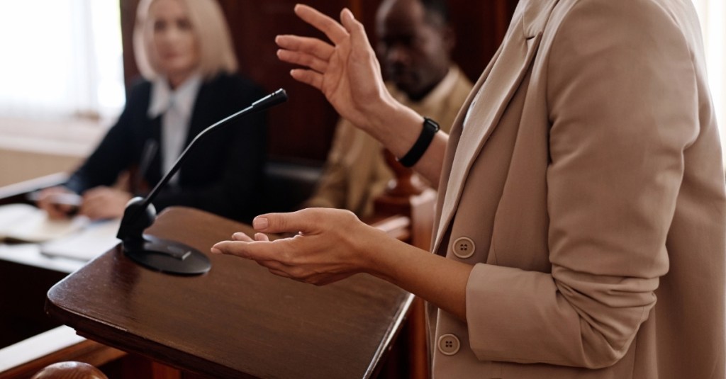 A woman standing at podium in a courtroom.