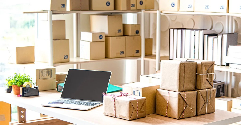 A storage room filled with boxes scattered all over and a laptop sitting on a desk.